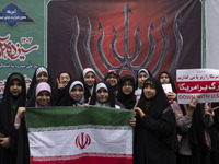 A group of veiled Iranian schoolgirls pose for a photograph while holding an Iranian flag in front of an anti-Israeli banner during an anti-...