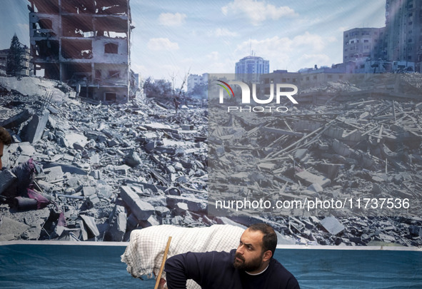 An Iranian man sits under a banner featuring a view of Gaza, which collapses due to Israeli airstrikes, during an anti-U.S. and anti-Israel...