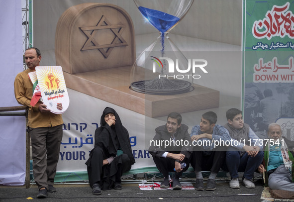 Iranian people sit in front of an anti-Israeli banner while participating in an anti-U.S. and anti-Israel rally marking the anniversary of t...