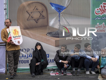 Iranian people sit in front of an anti-Israeli banner while participating in an anti-U.S. and anti-Israel rally marking the anniversary of t...