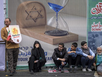 Iranian people sit in front of an anti-Israeli banner while participating in an anti-U.S. and anti-Israel rally marking the anniversary of t...