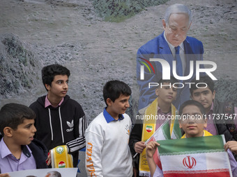 A group of Iranian schoolboys stands in front of a banner featuring a portrait of Israeli Prime Minister Benjamin Netanyahu during an anti-U...