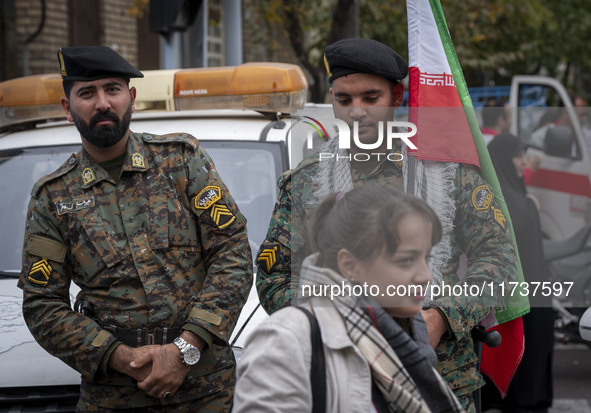 A young Iranian woman who does not wear a mandatory headscarf walks past two military personnel of the Iranian police special forces during...