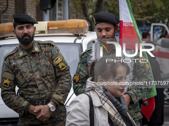 A young Iranian woman who does not wear a mandatory headscarf walks past two military personnel of the Iranian police special forces during...