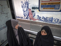 Two veiled Iranian women sit at a bustard in front of an anti-U.S. mural during an anti-U.S. and anti-Israel rally marking the anniversary o...