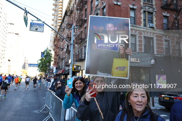 Crowds hold up signs and watch New York City marathon runners as they race up First Avenue in the Upper East Side neighborhood of New York,...