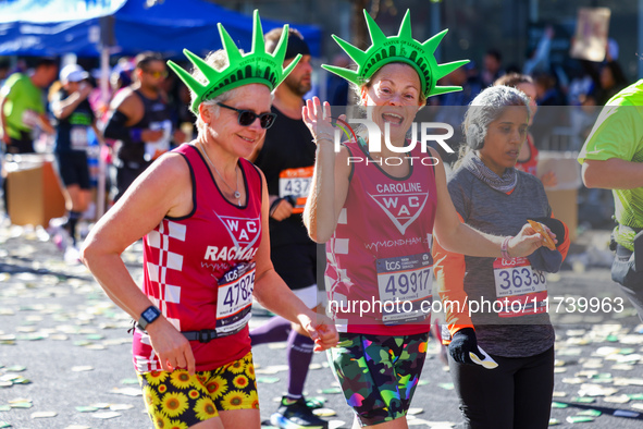 Two runners wearing Statue of Liberty foam headdresses smile as they notice the camera lens pointed at them while running up First Avenue du...