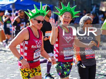 Two runners wearing Statue of Liberty foam headdresses smile as they notice the camera lens pointed at them while running up First Avenue du...