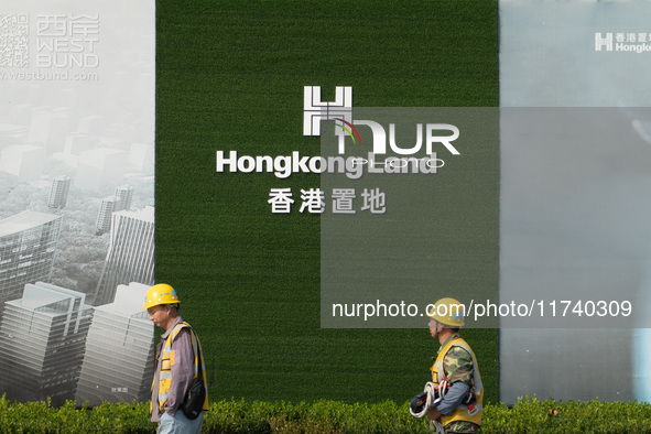 Workers pass by the construction site of the West Bund Financial City near the Hongkong Land corporate logo outside the fence in Shanghai, C...