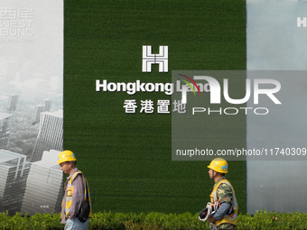 Workers pass by the construction site of the West Bund Financial City near the Hongkong Land corporate logo outside the fence in Shanghai, C...