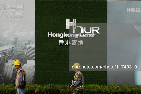 Workers pass by the construction site of the West Bund Financial City near the Hongkong Land corporate logo outside the fence in Shanghai, C...