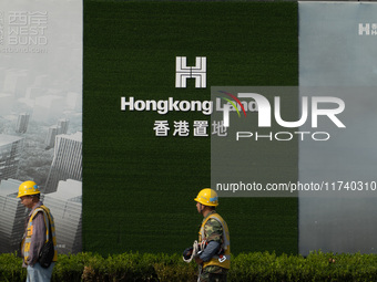 Workers pass by the construction site of the West Bund Financial City near the Hongkong Land corporate logo outside the fence in Shanghai, C...