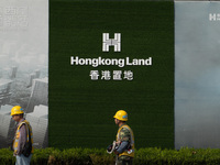 Workers pass by the construction site of the West Bund Financial City near the Hongkong Land corporate logo outside the fence in Shanghai, C...