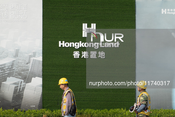 Workers pass by the construction site of the West Bund Financial City near the Hongkong Land corporate logo outside the fence in Shanghai, C...