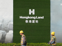 Workers pass by the construction site of the West Bund Financial City near the Hongkong Land corporate logo outside the fence in Shanghai, C...