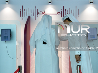 An official assists a Qatari voter in casting their electronic vote at a polling station in a general referendum on constitutional amendment...