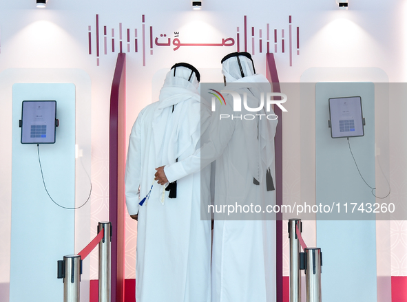 An official assists a Qatari voter in casting their electronic vote at a polling station in a general referendum on constitutional amendment...