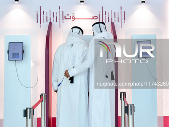 An official assists a Qatari voter in casting their electronic vote at a polling station in a general referendum on constitutional amendment...