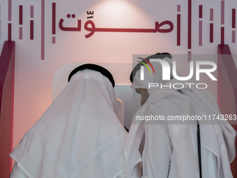 An official assists a Qatari voter in casting their electronic vote at a polling station in a general referendum on constitutional amendment...