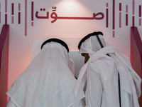 An official assists a Qatari voter in casting their electronic vote at a polling station in a general referendum on constitutional amendment...