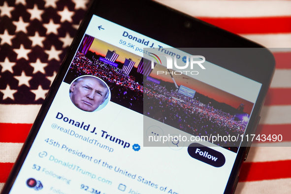 Donald J. Trump social media site on X, formerly known as Twitter, is displayed on a mobile phone screen with US flag in the background for...