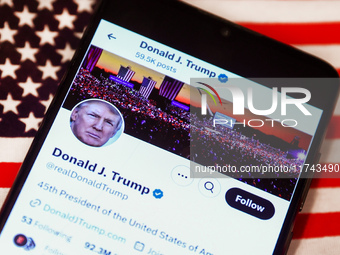 Donald J. Trump social media site on X, formerly known as Twitter, is displayed on a mobile phone screen with US flag in the background for...