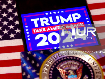 'Trump Take America Back' sign is displayed on a mobile phone screen with US flag in the background for illustration photo. Krakow, Poland o...