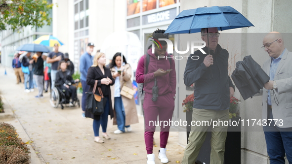 A group of people waits outside 125 S Jefferson St, Chicago, IL, to vote in the 2024 Presidential election. It is raining, so some of them h...