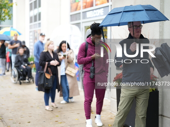 A group of people waits outside 125 S Jefferson St, Chicago, IL, to vote in the 2024 Presidential election. It is raining, so some of them h...