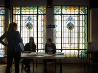 A voter picks up her ballot to vote for President, Congress, and local races for the 2024 election in a room with stained glass windows at t...