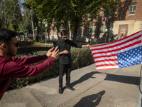 An Iranian man holds the U.S. flag, which hangs upside down, while his friend takes photographs during their visit to the former U.S. embass...