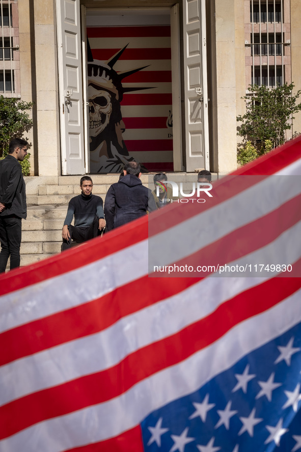 A group of Iranian men gathers behind the U.S. flag, which is hung upside down, and under an anti-U.S. mural while visiting the former U.S....