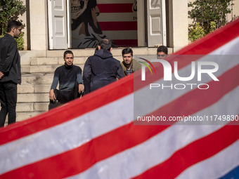 A group of Iranian men gathers behind the U.S. flag, which is hung upside down, and under an anti-U.S. mural while visiting the former U.S....