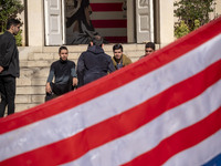 A group of Iranian men gathers behind the U.S. flag, which is hung upside down, and under an anti-U.S. mural while visiting the former U.S....