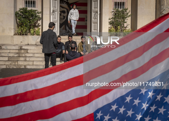 A group of Iranian men gathers behind the U.S. flag, which is hung upside down, and under an anti-U.S. mural while visiting the former U.S....