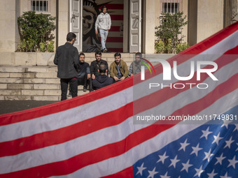 A group of Iranian men gathers behind the U.S. flag, which is hung upside down, and under an anti-U.S. mural while visiting the former U.S....