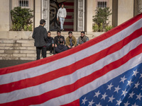 A group of Iranian men gathers behind the U.S. flag, which is hung upside down, and under an anti-U.S. mural while visiting the former U.S....