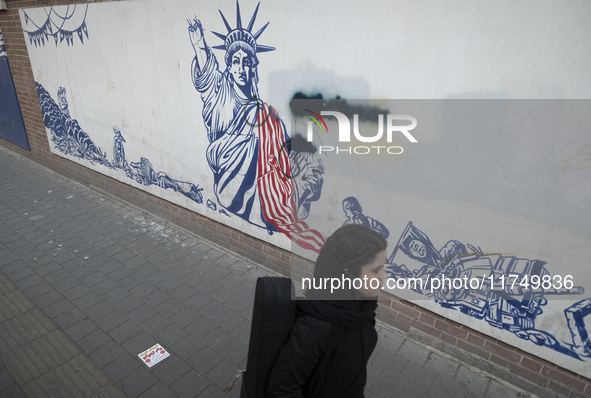 A young Iranian woman walks past an anti-U.S. mural on a wall of the former U.S. embassy in Tehran, Iran, on November 7, 2024. Former U.S. P...