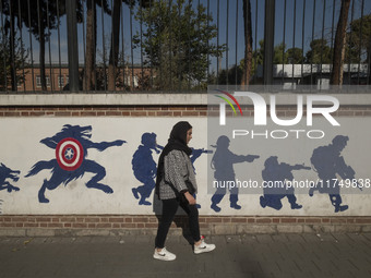 A young Iranian woman walks past an anti-U.S. mural on a wall of the former U.S. embassy in Tehran, Iran, on November 7, 2024. Former U.S. P...