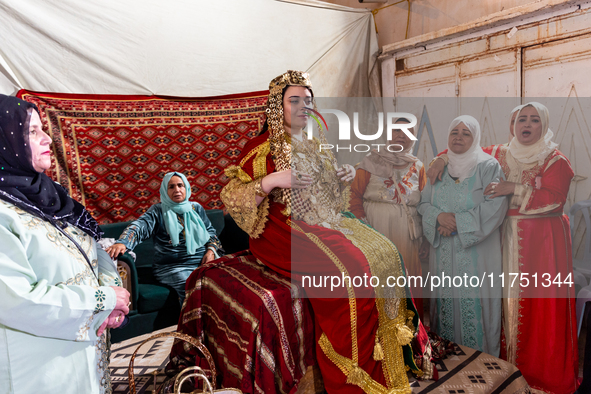 A bedouin bride dressed in traditional bedouin dress and head cover sits on a raised chair as she celebrates her wedding together with her f...