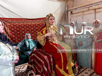 A bedouin bride dressed in traditional bedouin dress and head cover sits on a raised chair as she celebrates her wedding together with her f...