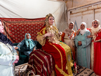 A bedouin bride dressed in traditional bedouin dress and head cover sits on a raised chair as she celebrates her wedding together with her f...