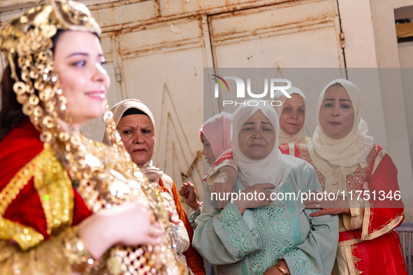 A bedouin bride dressed in traditional bedouin dress and head cover sits on a raised chair as she celebrates her wedding together with her f...