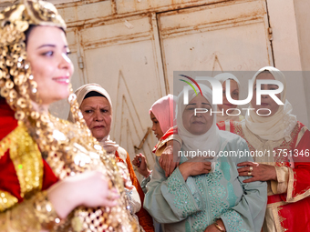 A bedouin bride dressed in traditional bedouin dress and head cover sits on a raised chair as she celebrates her wedding together with her f...