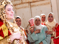 A bedouin bride dressed in traditional bedouin dress and head cover sits on a raised chair as she celebrates her wedding together with her f...