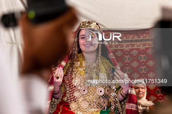 A bedouin bride dressed in traditional bedouin dress and head cover sits on a raised chair as she celebrates her wedding together with her f...