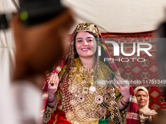 A bedouin bride dressed in traditional bedouin dress and head cover sits on a raised chair as she celebrates her wedding together with her f...