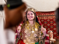 A bedouin bride dressed in traditional bedouin dress and head cover sits on a raised chair as she celebrates her wedding together with her f...