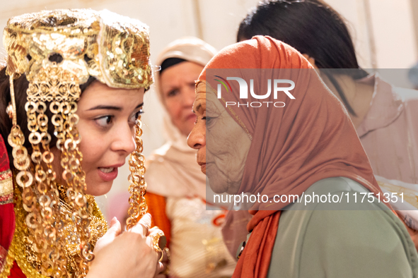 A bedouin bride dressed in traditional bedouin dress and head cover sits on a raised chair as she celebrates her wedding together with her f...