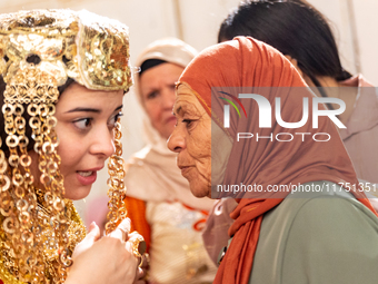 A bedouin bride dressed in traditional bedouin dress and head cover sits on a raised chair as she celebrates her wedding together with her f...